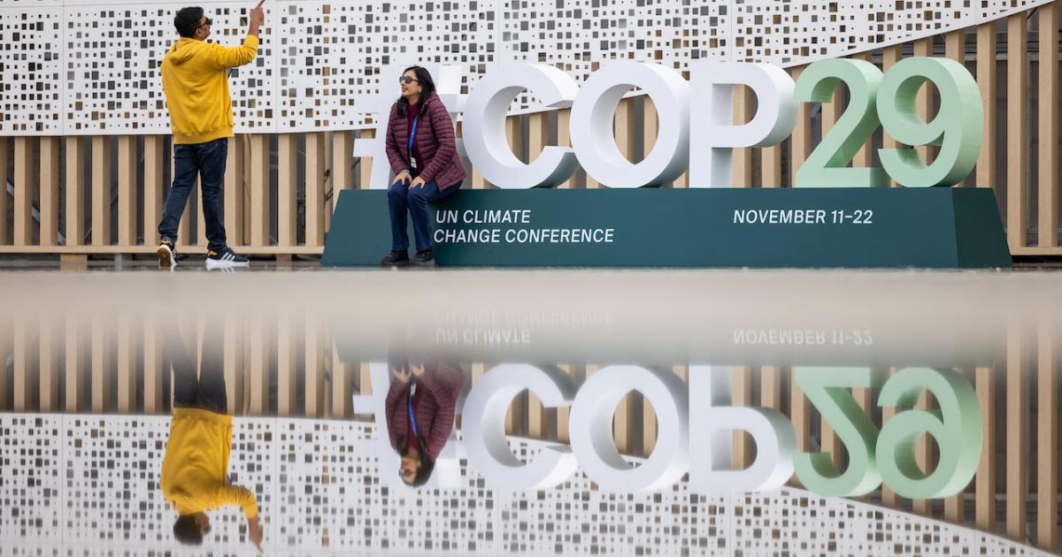 Dos personas se hacen fotos a la entrada del edificio en el que se celebrará la cumbre de la ONU sobre el cambio climático en Bakú.